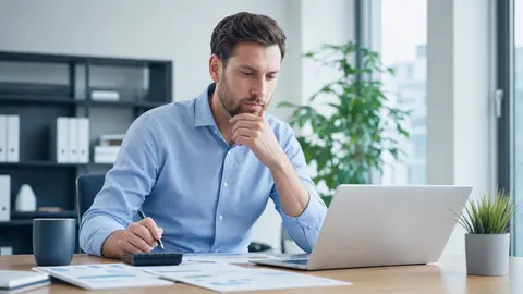 Kostenfaktoren einer Prozessautomatisierung: Unternehmerin kalkuliert am Laptop mit Taschenrechner das Budget für ein Automatisierungsprojekt