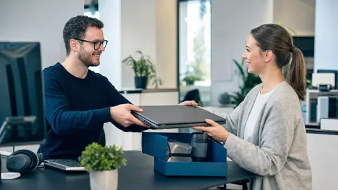 Mitarbeiter-Onboarding automatisieren: IT-Administrator übergibt einer neuen Mitarbeiterin am ersten Arbeitstag den fertig eingerichteten Business-Laptop